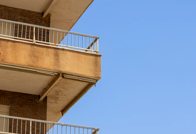 Brown apartment building balconies seen from below against a clear blue sky