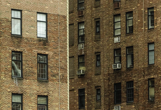 Two brick apartment buildings with many windows and air conditioners