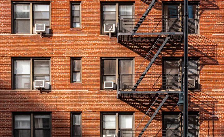 Red brick apartment building with a black metal fire escape and window air conditioners