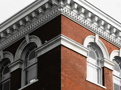 Corner of a brick building with arched windows and its roofline against the sky