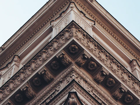 Ornate carved cornice at the upper corner of an old building against a blue sky