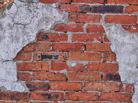 Old brick wall with cracks running through the brick and gray cement patches