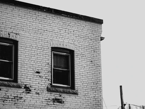 Corner of a weathered brick building with two windows, where cracks from a failing lintel often start at the window corners