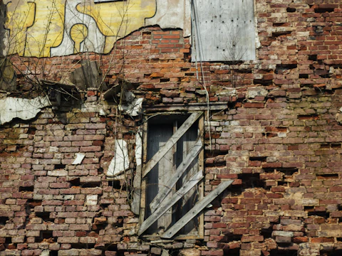 Old brick building with a broken window and damaged masonry around the opening