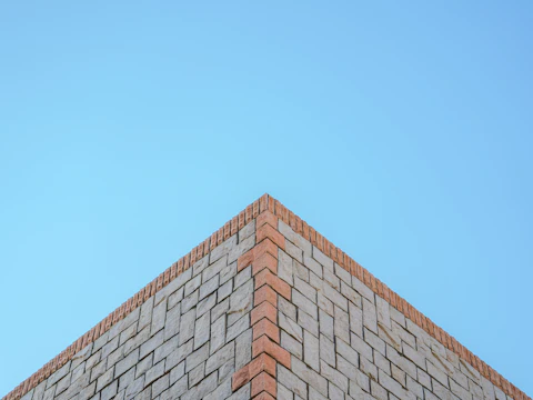 Top corner of a brick wall against the sky, where a parapet lean or bow shows first