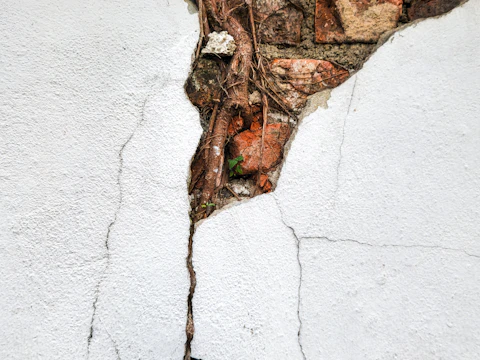 Deep crack running across a weathered wall, exposing the brickwork underneath