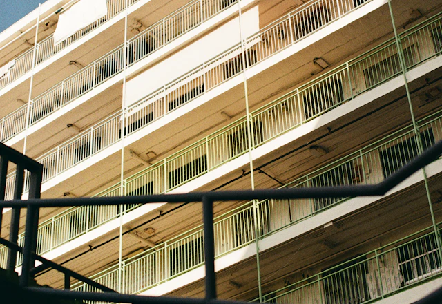 Apartment building with white balconies and green railings against a blue sky