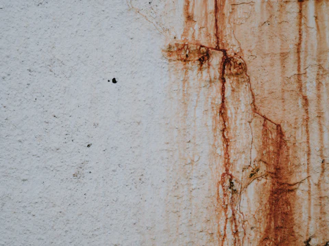 Orange rust stain running down a pale masonry wall from corroding steel embedded behind it