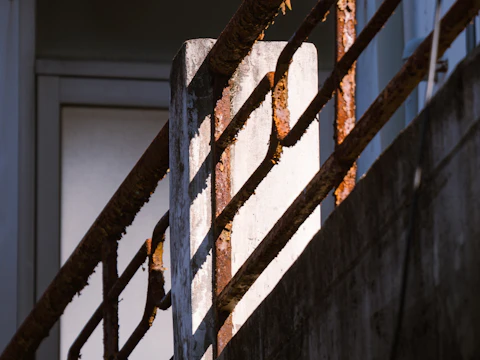 Rusted metal railing set on a concrete post in bright sunlight