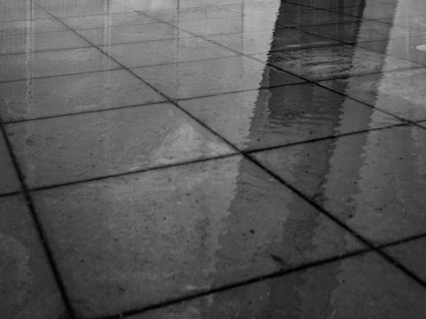 Wet tiled ground outside a glass door, with the building reflected in the water